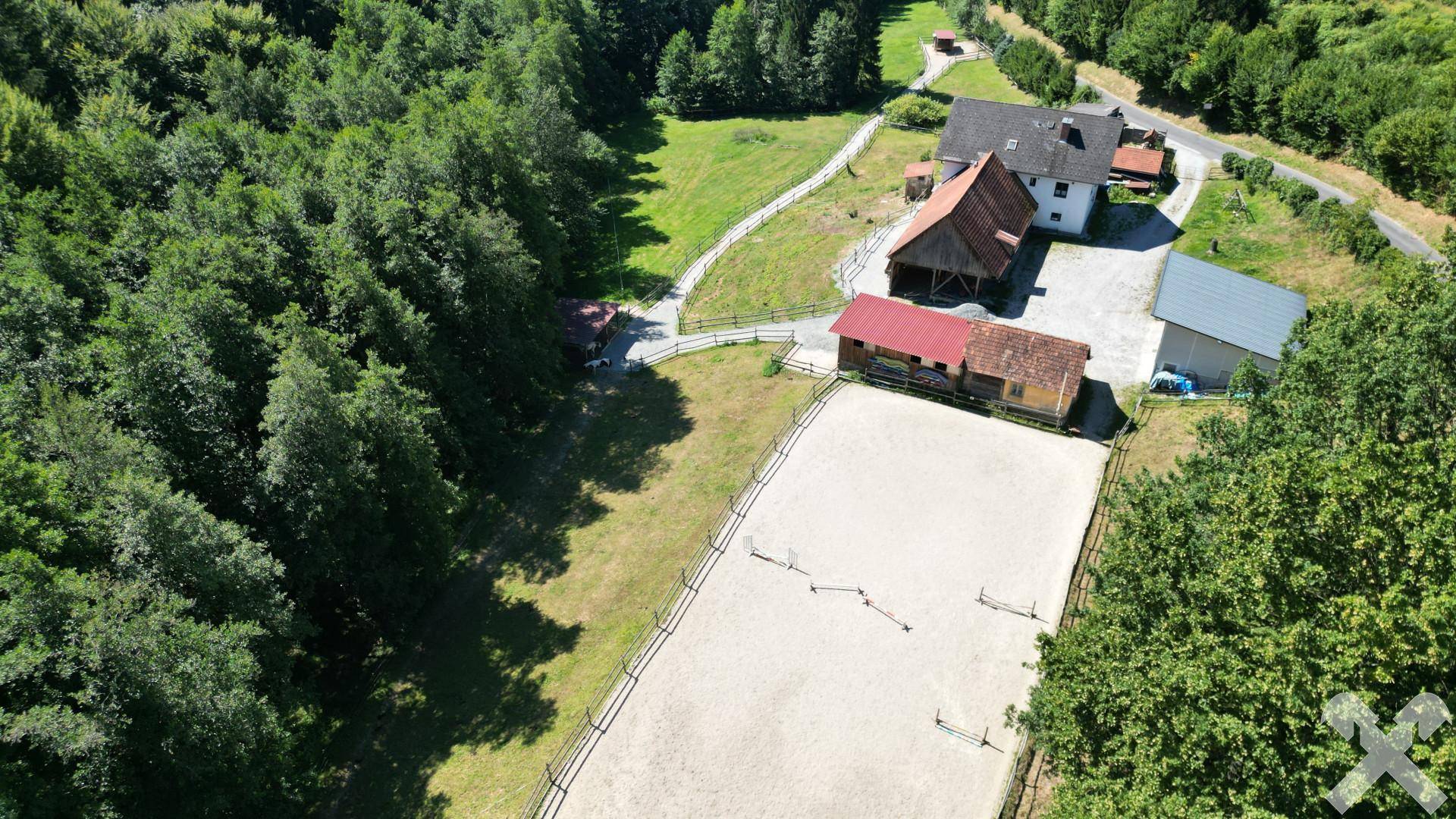 Luftaufnahme des Reitplatzes und der angrenzenden Wirtschaftsgebäude, eingebettet in die Natur.