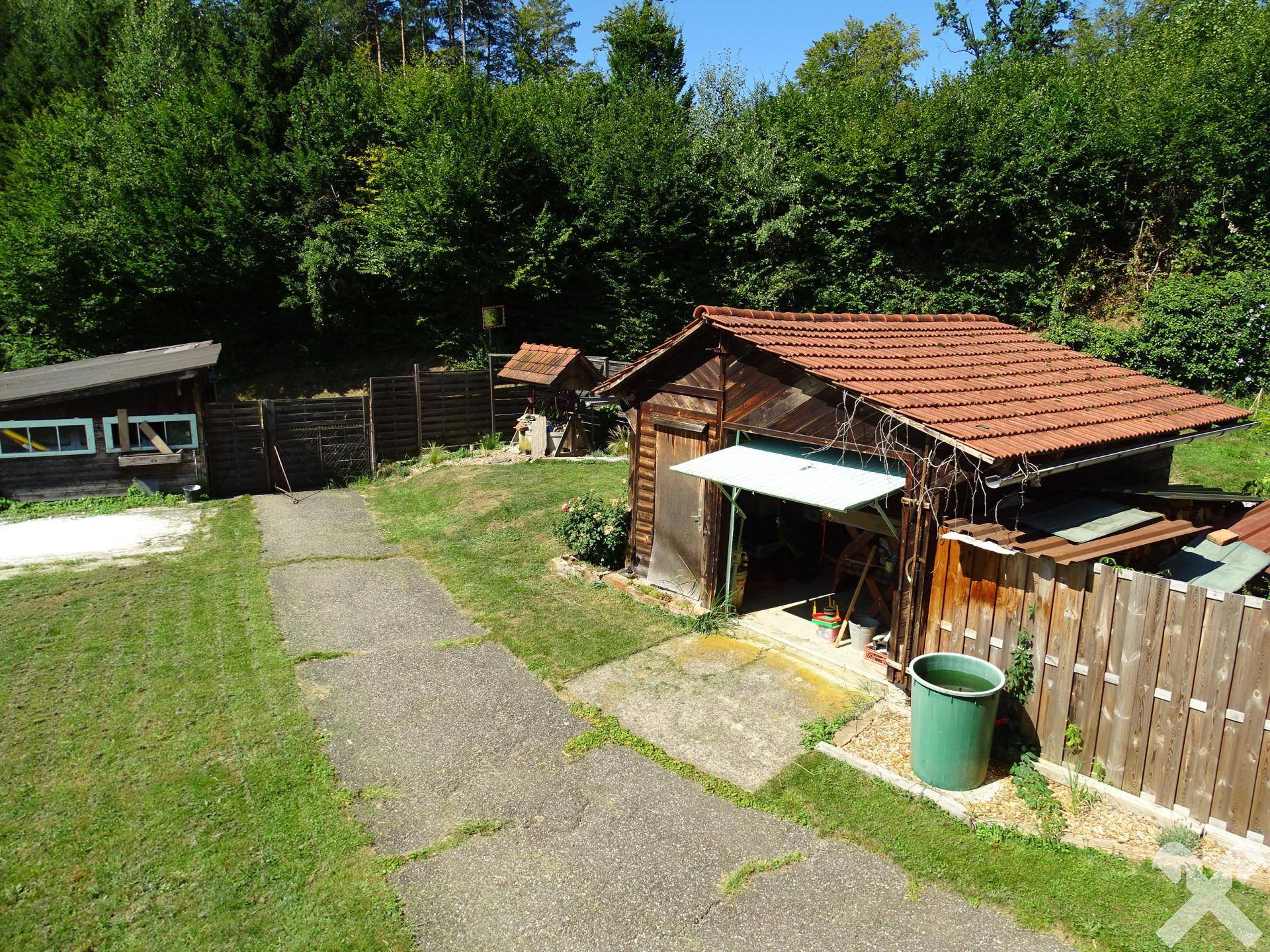 Rustikale Holzschuppen und ein gepflasterter Weg in einer ländlichen Umgebung mit viel Grün.
