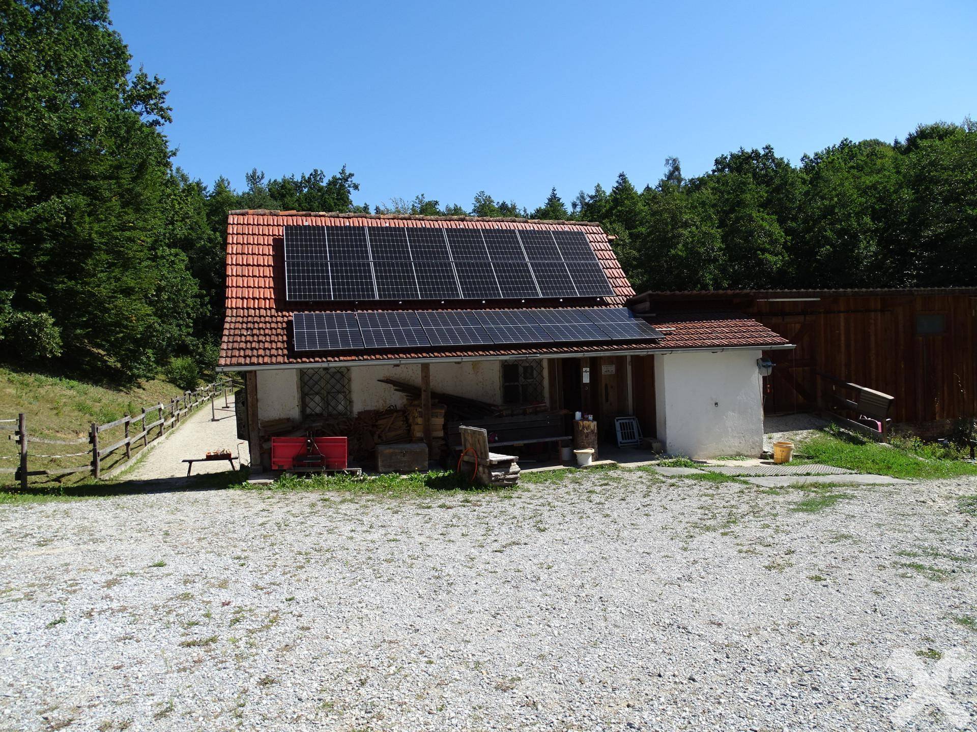 Kleineres Wirtschaftsgebäude mit Ziegeldach und mehreren Solarmodulen, umgeben von Schotter.