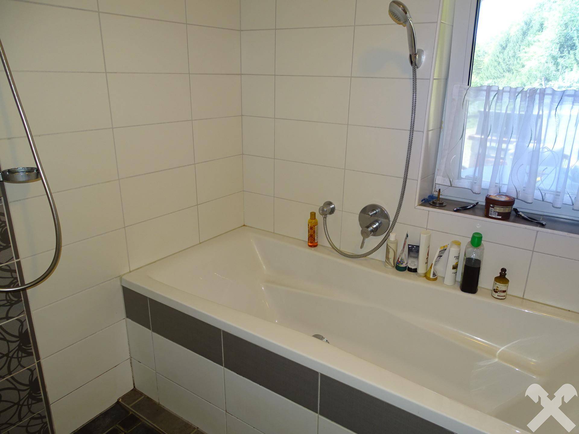 Badewanne mit weißen Fliesen und einem Fenster, das Tageslicht hereinlässt.