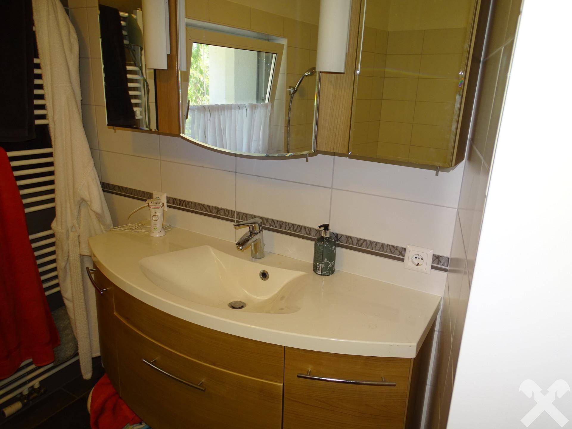 Waschbecken mit Holzunterschrank und Spiegelschrank in einem hell gefliesten Badezimmer.