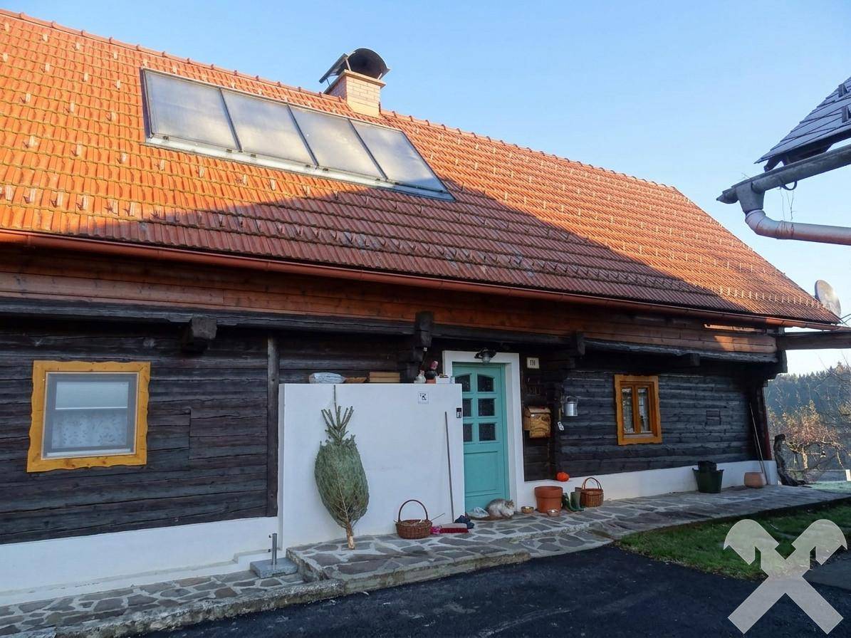 Rustikales Holzhaus mit rotem Ziegeldach, Solarpaneelen und einer hellblauen Eingangstür.