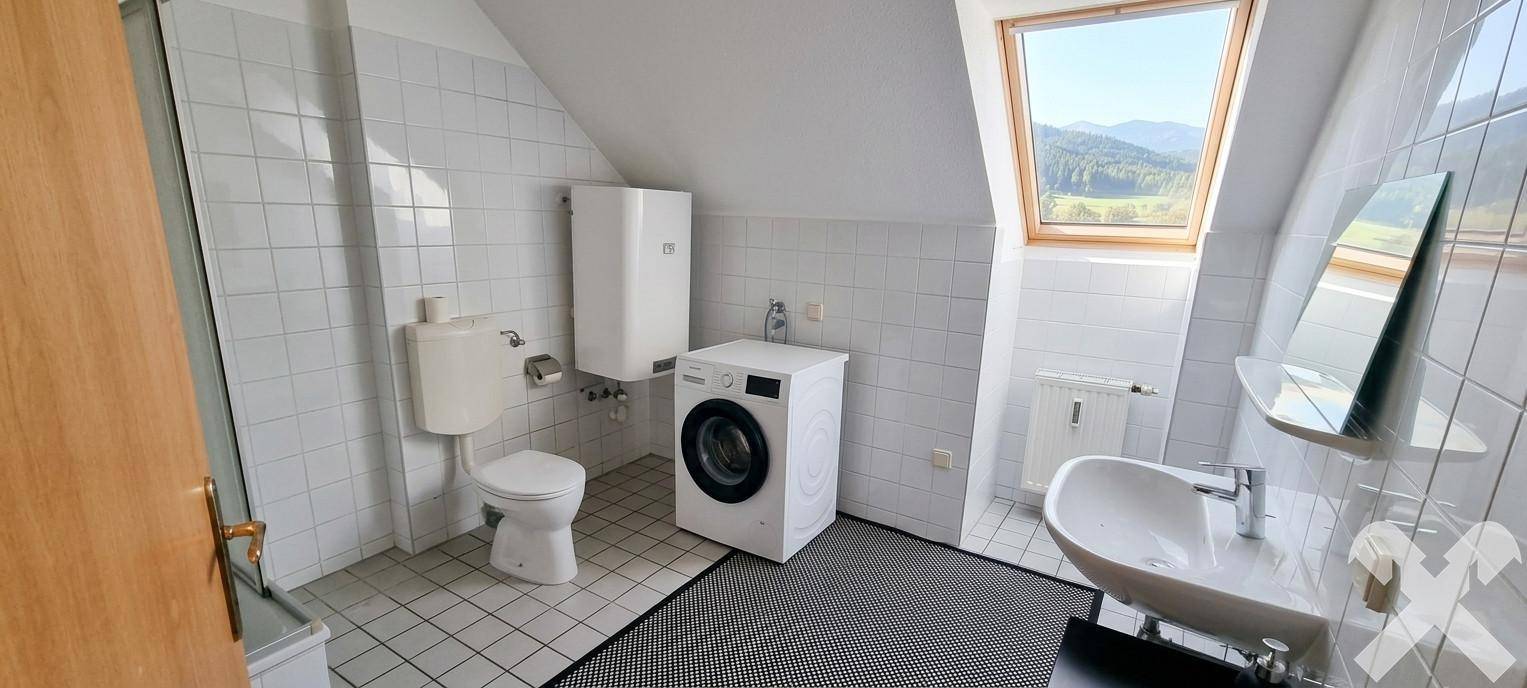 Modernes Badezimmer im Dachgeschoss mit Schrägdachfenster, WC und Waschmaschine.