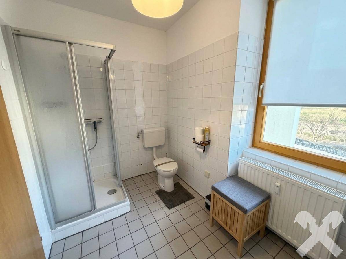 Badezimmer mit Duschkabine, WC, Fliesenboden und Fenster für natürliche Belüftung.