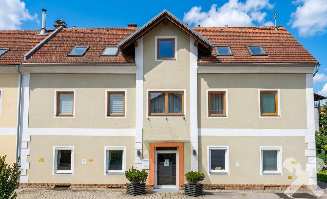 Gepflegte Gebäudefassade im traditionellen Stil mit Dachfenstern und gepflastertem Vorplatz.