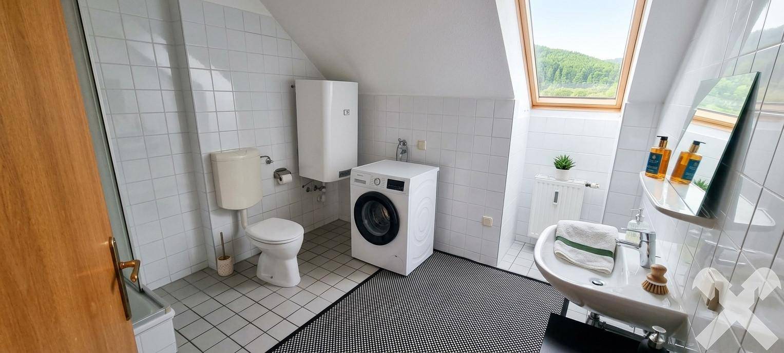 Helles Badezimmer mit weißen Fliesen, Waschmaschine und großem Dachfenster.