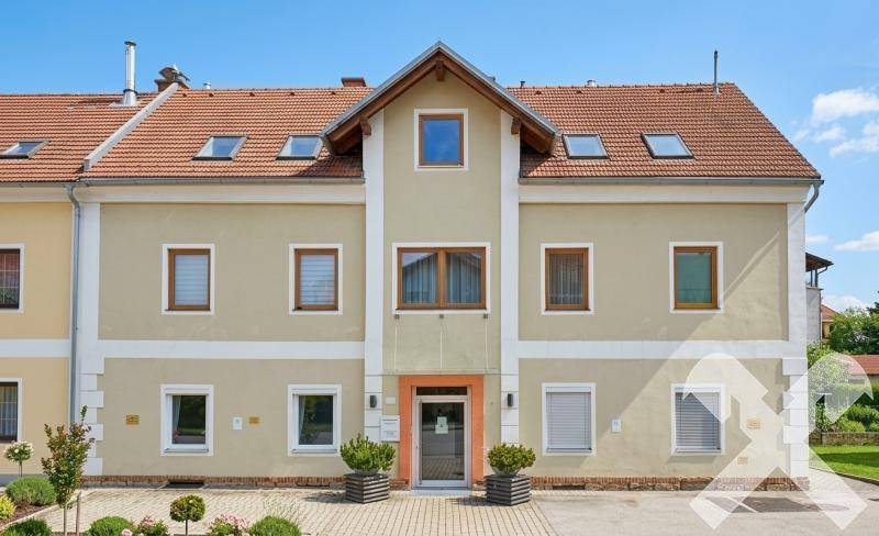 Vorderansicht des Gebäudes mit hellbeiger Fassade, roten Dachziegeln und gepflegtem Vorgarten.