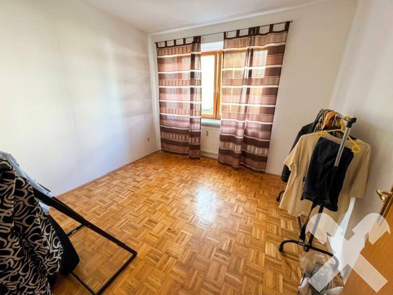 Schlafzimmer mit Parkettboden, Fenster und gestreiften Vorhängen.
