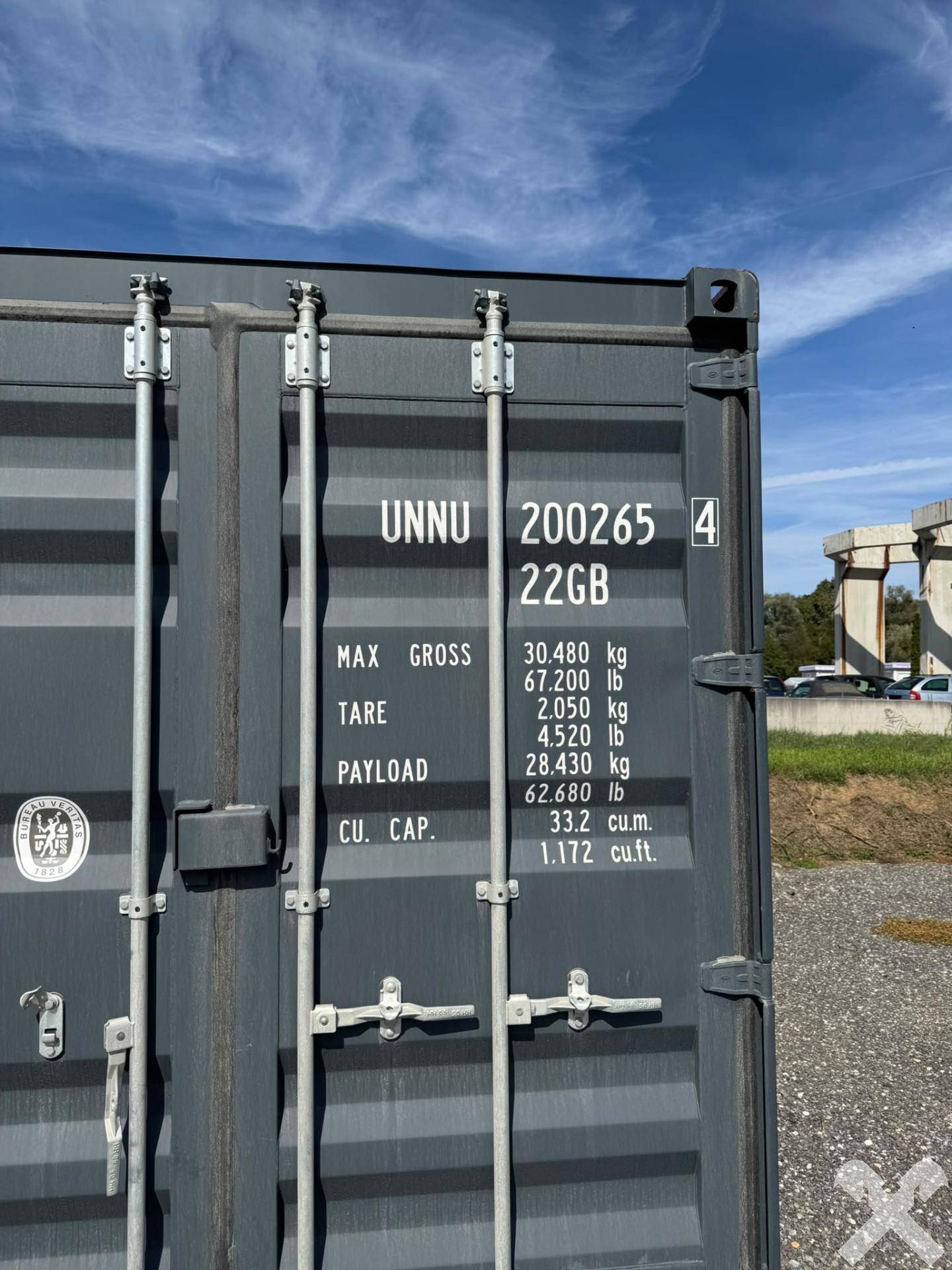 Nahaufnahme der Seite eines dunkelgrauen Schiffscontainers mit technischen Beschriftungen.
