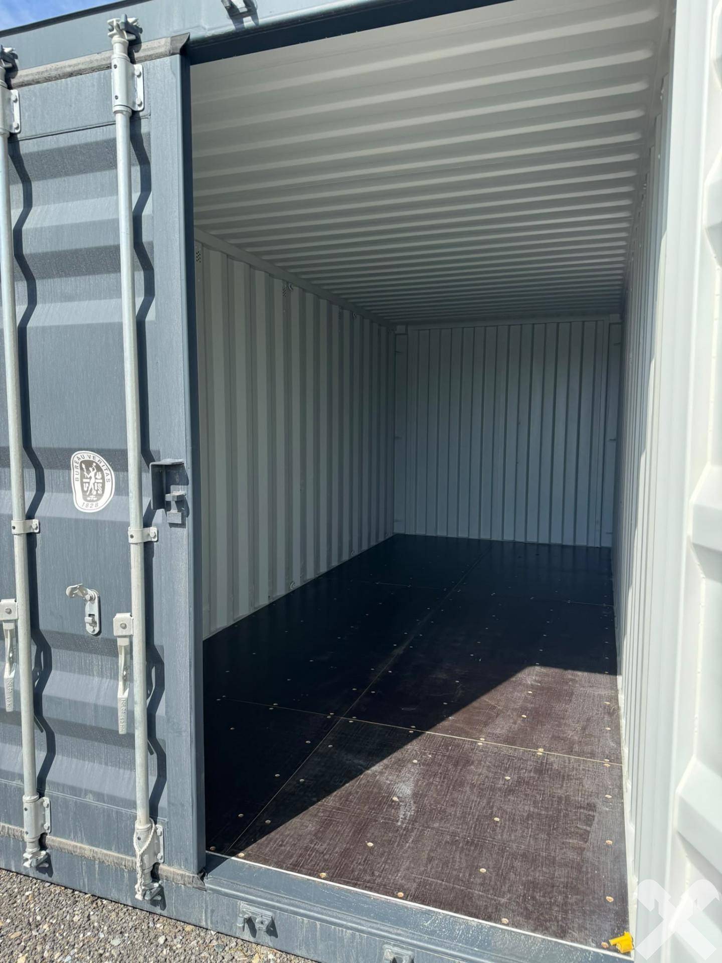 Blick in das leere Innere eines geöffneten Schiffscontainers mit Holzboden und Wellblechwänden.