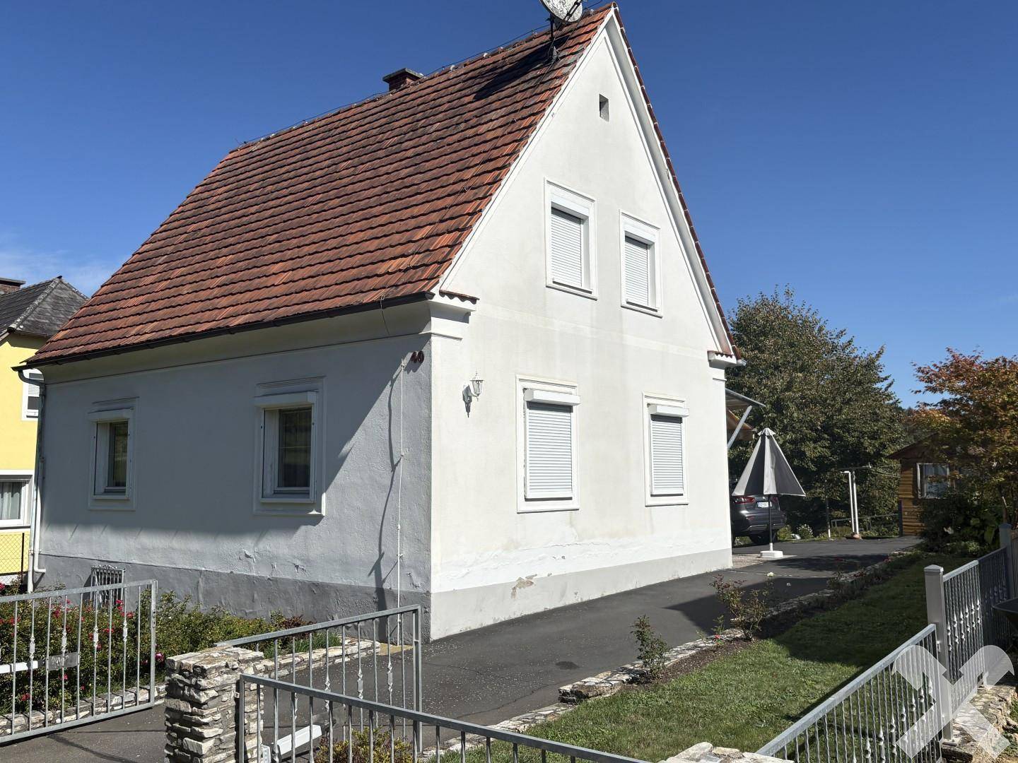 Seitenansicht des Einfamilienhauses mit weißer Fassade, Ziegeldach und einer Zufahrt zum Grundstück.