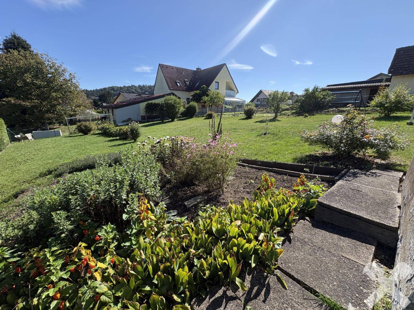 Großer Gartenbereich mit Blumenbeeten, Rasenfläche und Blick auf die umliegende Landschaft.