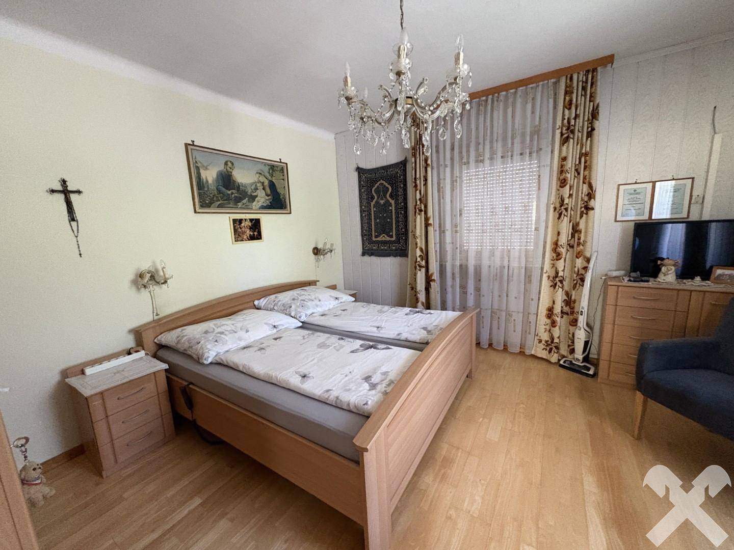 Schlafzimmer mit Doppelbett, Holzmöbeln, Parkettboden und einem Kronleuchter an der Decke.