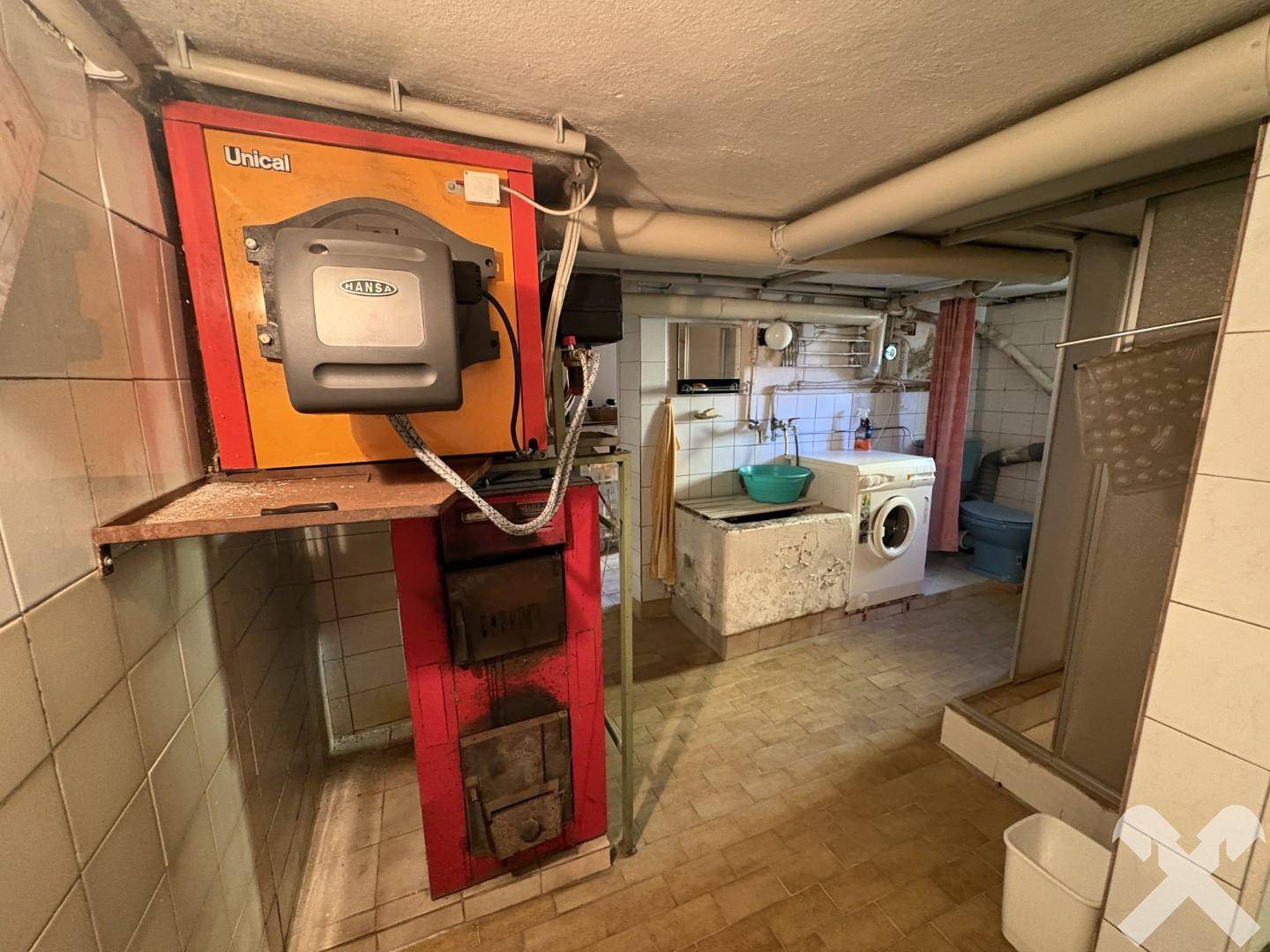 Kellerraum mit Heizungsanlage, Waschmaschine, Waschbecken und gefliestem Boden.