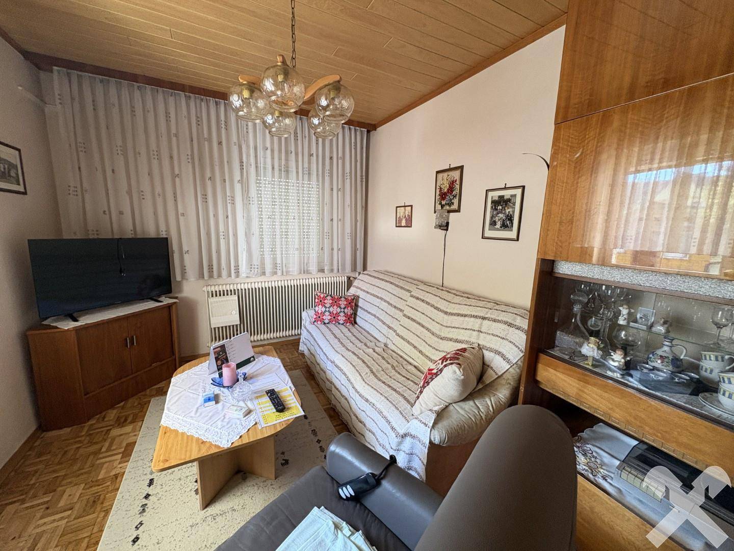 Wohnzimmer mit Sofa, Couchtisch, Holzdecke und einem großen Schrank mit Vitrine.