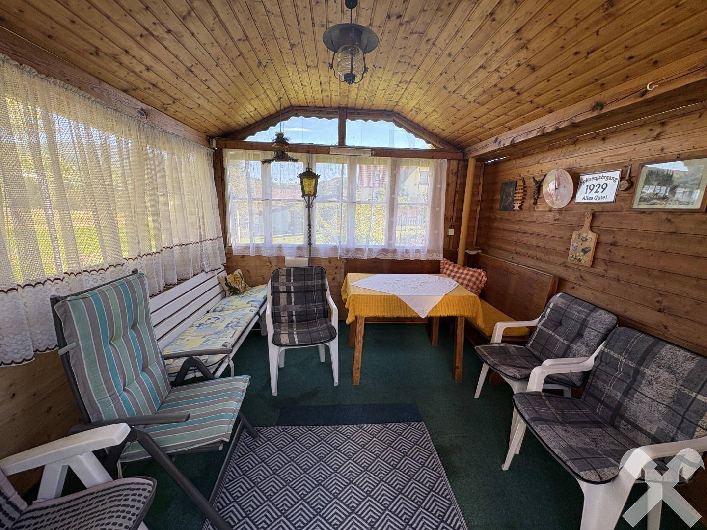 Gemütlicher Wintergarten mit Holzvertäfelung, Fenstern und einer Sitzgruppe für entspannte Stunden.