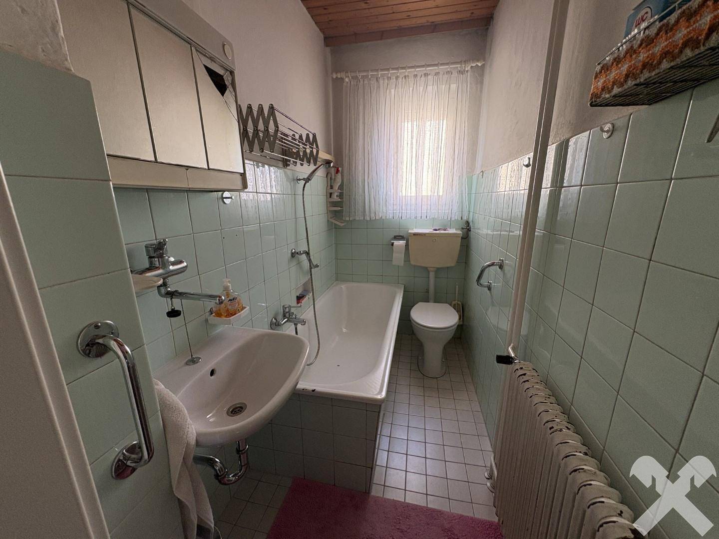 Badezimmer mit hellgrünen Fliesen, Badewanne, Toilette, Waschbecken und einem Fenster.