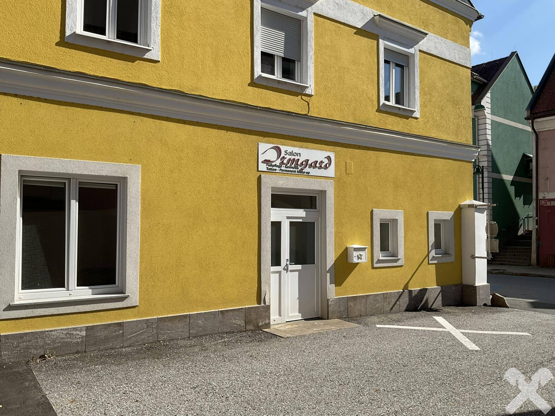 Detaillierte Ansicht der gelben Gebäudefassade mit Eingangstür, Fenstern und einem Briefkasten im Sonnenlicht.