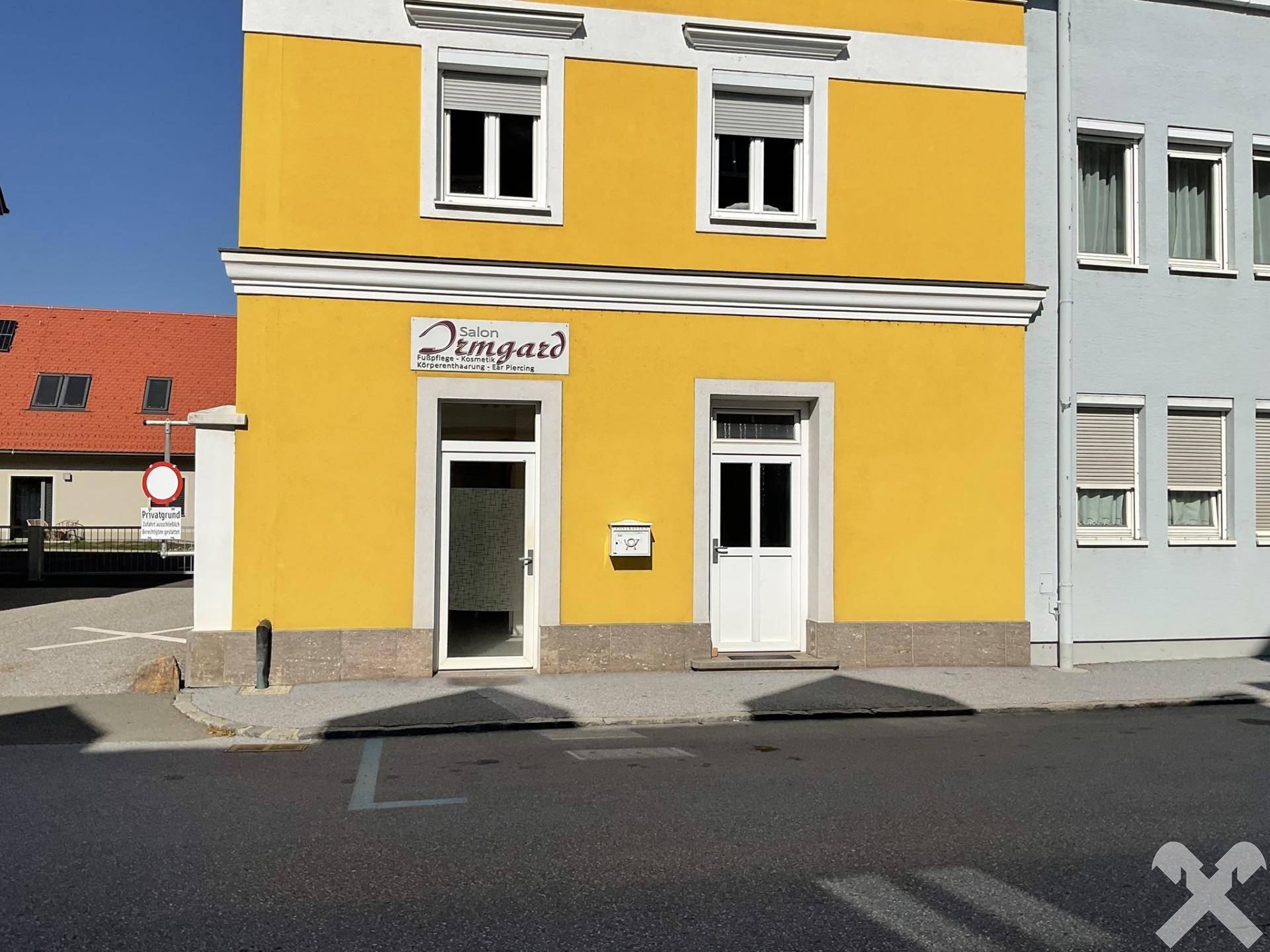 Nahaufnahme der gelben Fassade mit zwei Eingangstüren und Fenstern im Erdgeschoss an einem sonnigen Tag.