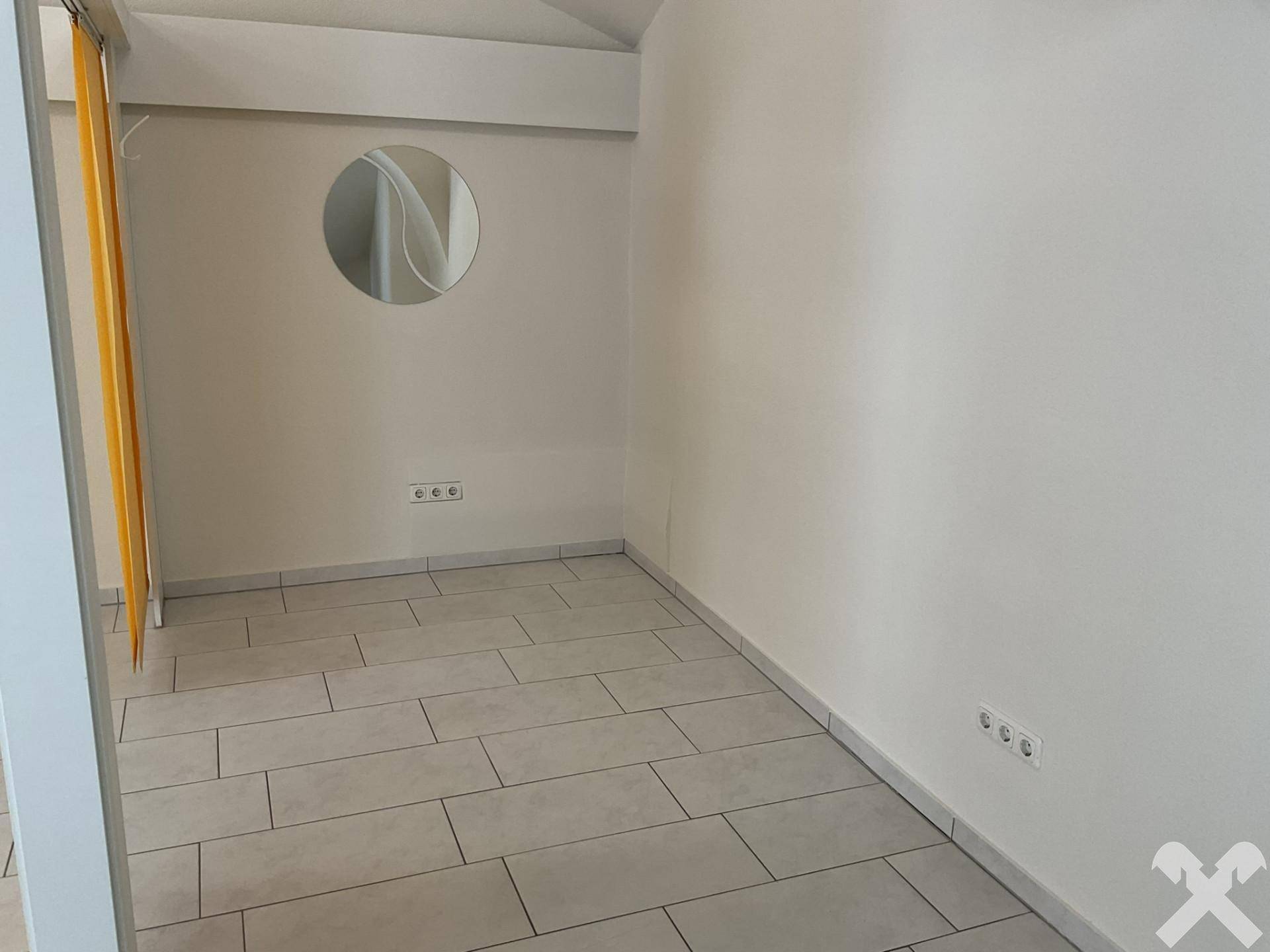 Ecke eines Raumes mit Fliesenboden, hellen Wänden und einem runden Spiegel an der Wand, der den Raum erweitert.