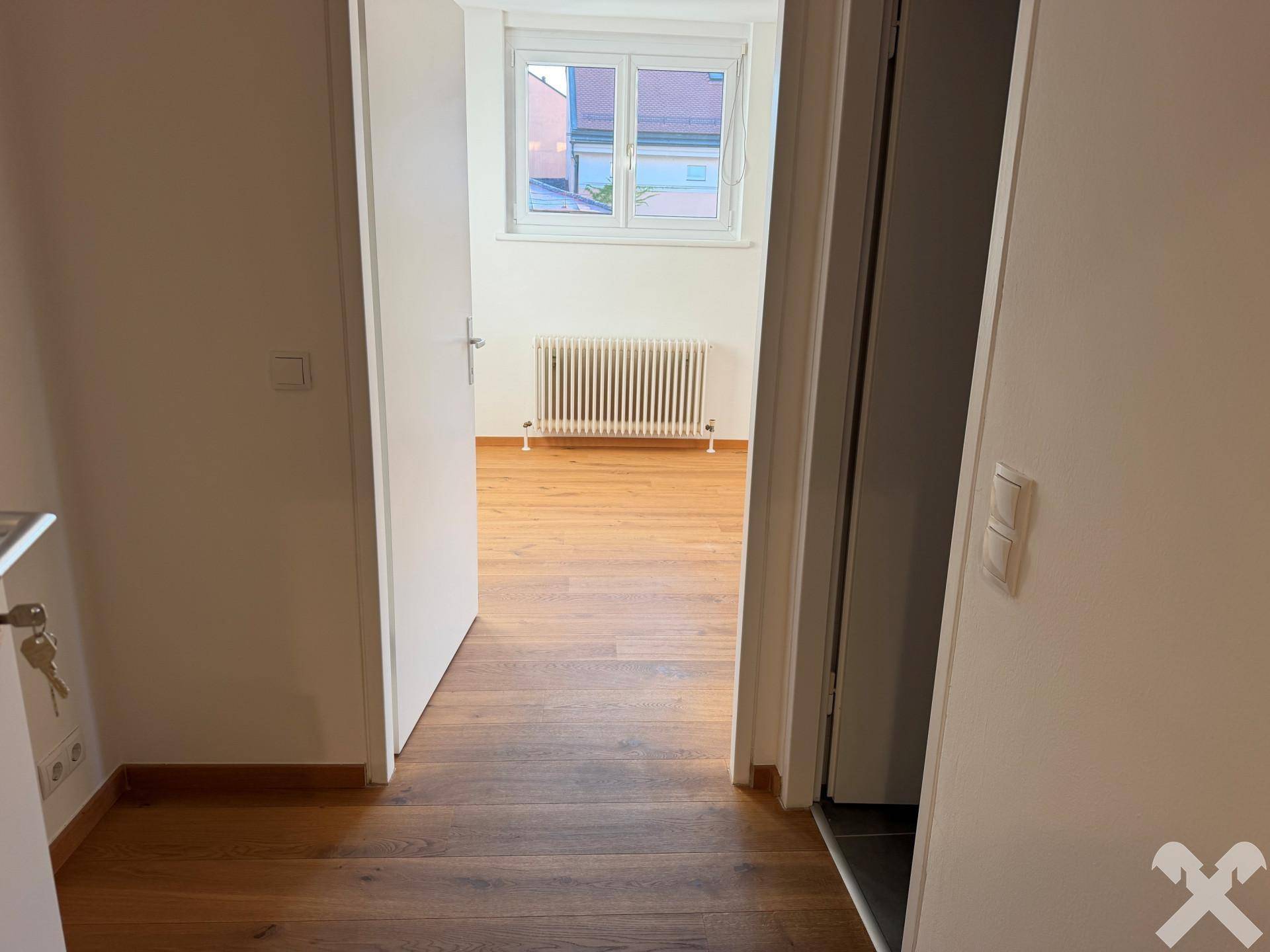 Blick durch eine offene Tür in einen weiteren hellen Raum mit Holzboden.