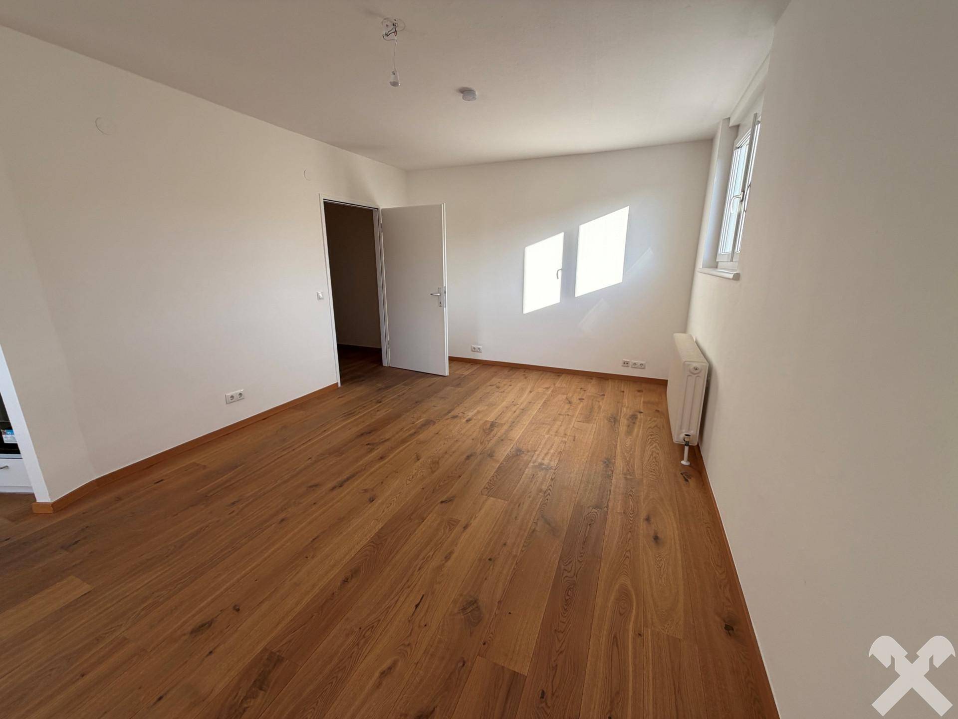 Geräumiger, heller Raum mit Holzboden und Fenster, ideal als Wohn- oder Schlafzimmer.