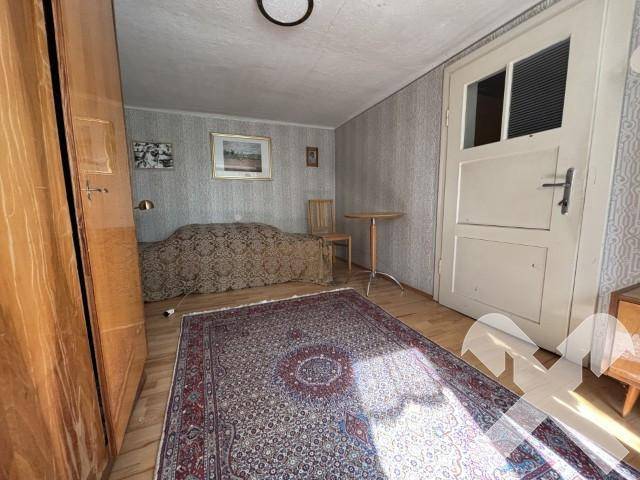 Einfaches Schlafzimmer mit Holzboden, Kleiderschrank und traditionellem Teppich.
