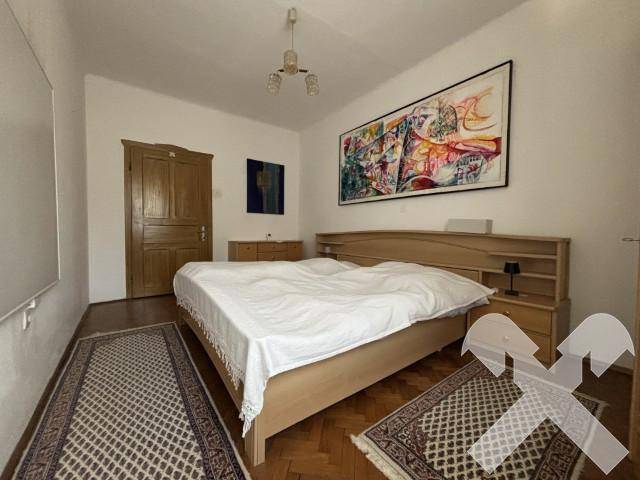 Helles Schlafzimmer mit Holzbett, Parkettboden und einem modernen Kunstwerk an der Wand.