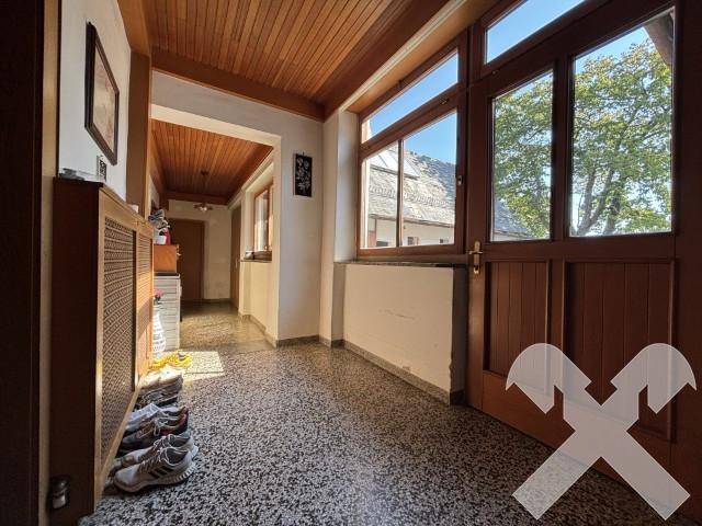 Heller Flur mit Terrazzoboden, Holzdecke und großem Fenster zur Außenseite.