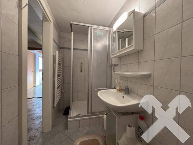 Kleines Badezimmer mit Duschkabine, Waschbecken und beheiztem Handtuchhalter.