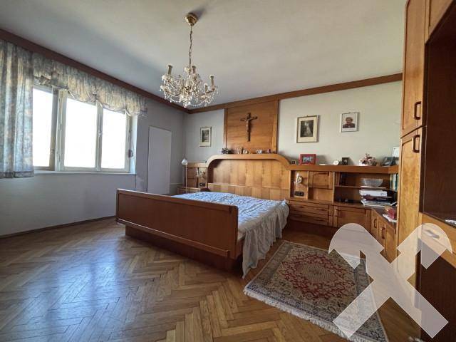 Geräumiges Schlafzimmer mit Holzbett, Parkettboden und traditionellem Kronleuchter.
