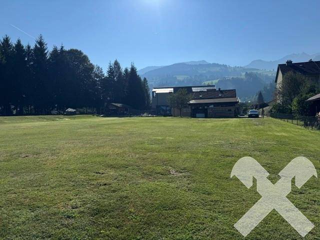 Ausgedehnte Grünfläche mit klarem Himmel und Panoramablick auf die Alpenregion und einige Häuser.