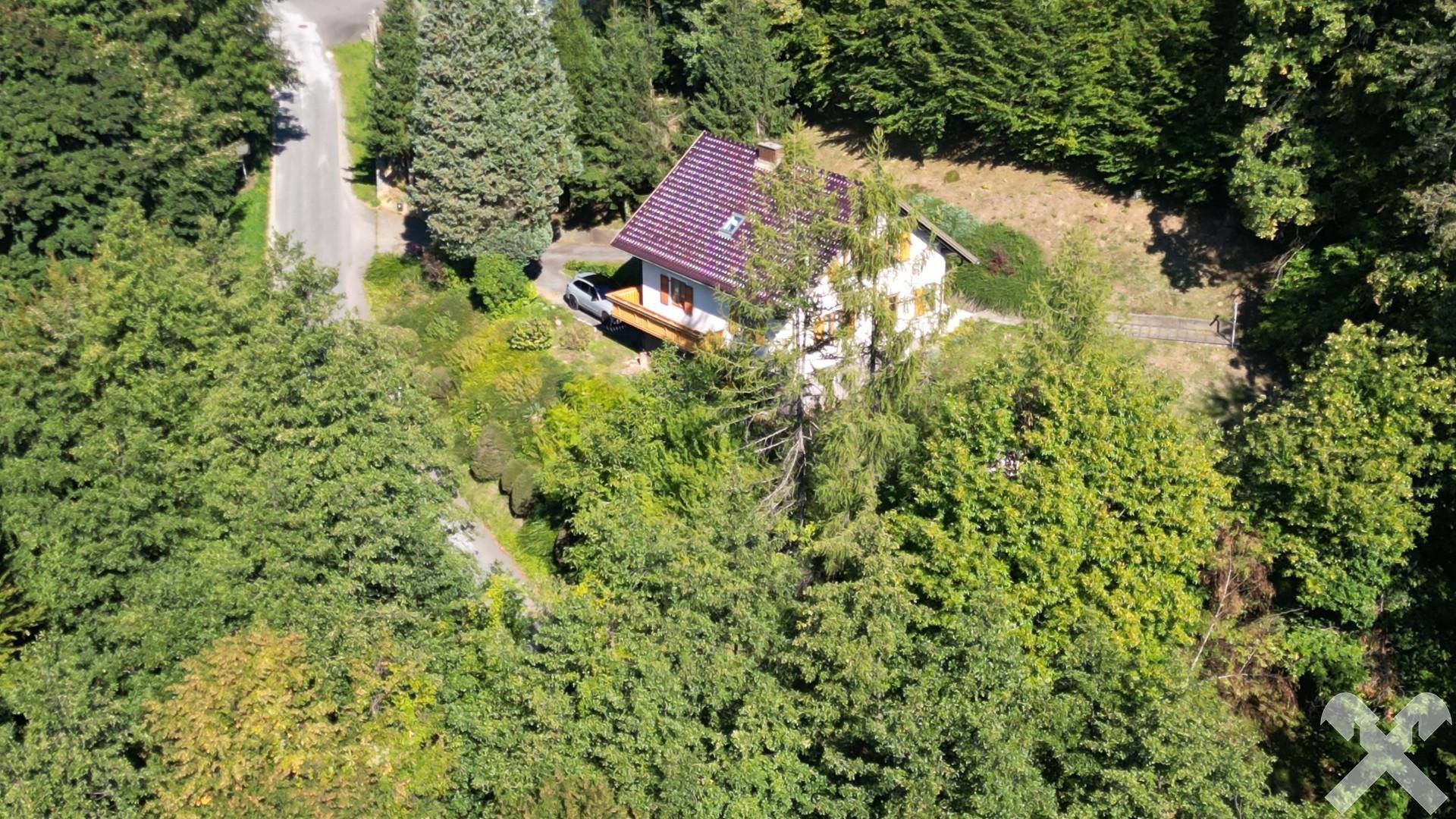 Weitläufige Luftansicht eines Hauses in ländlicher Umgebung, eingebettet in dichte Wälder und grüne Hügel.