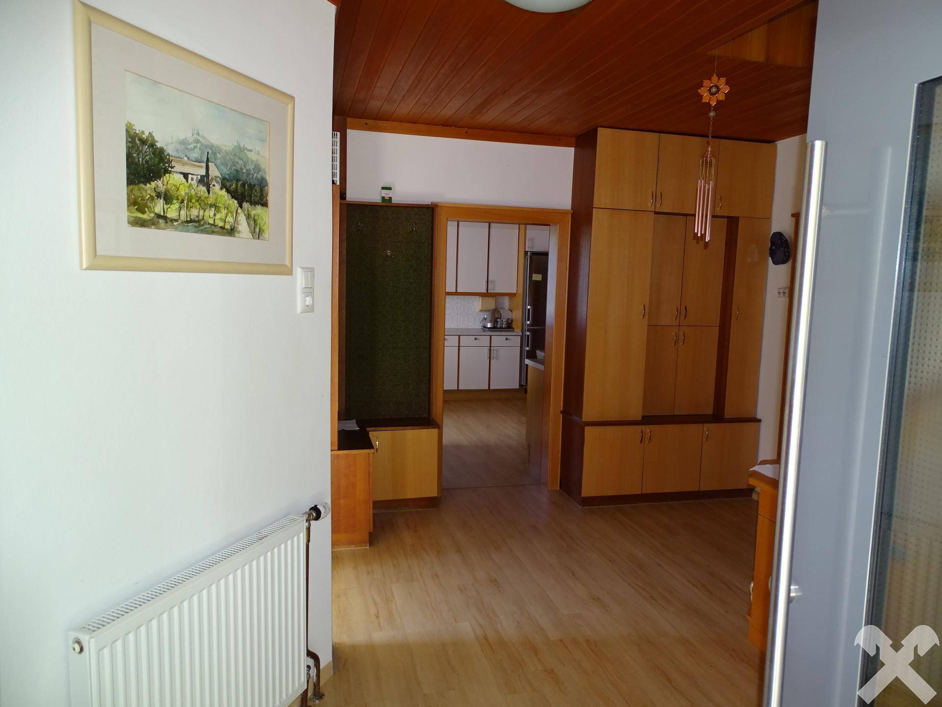 Eingangsbereich mit Holzdecke, Einbauschränken und hellem Laminatboden, der zur Küche führt.