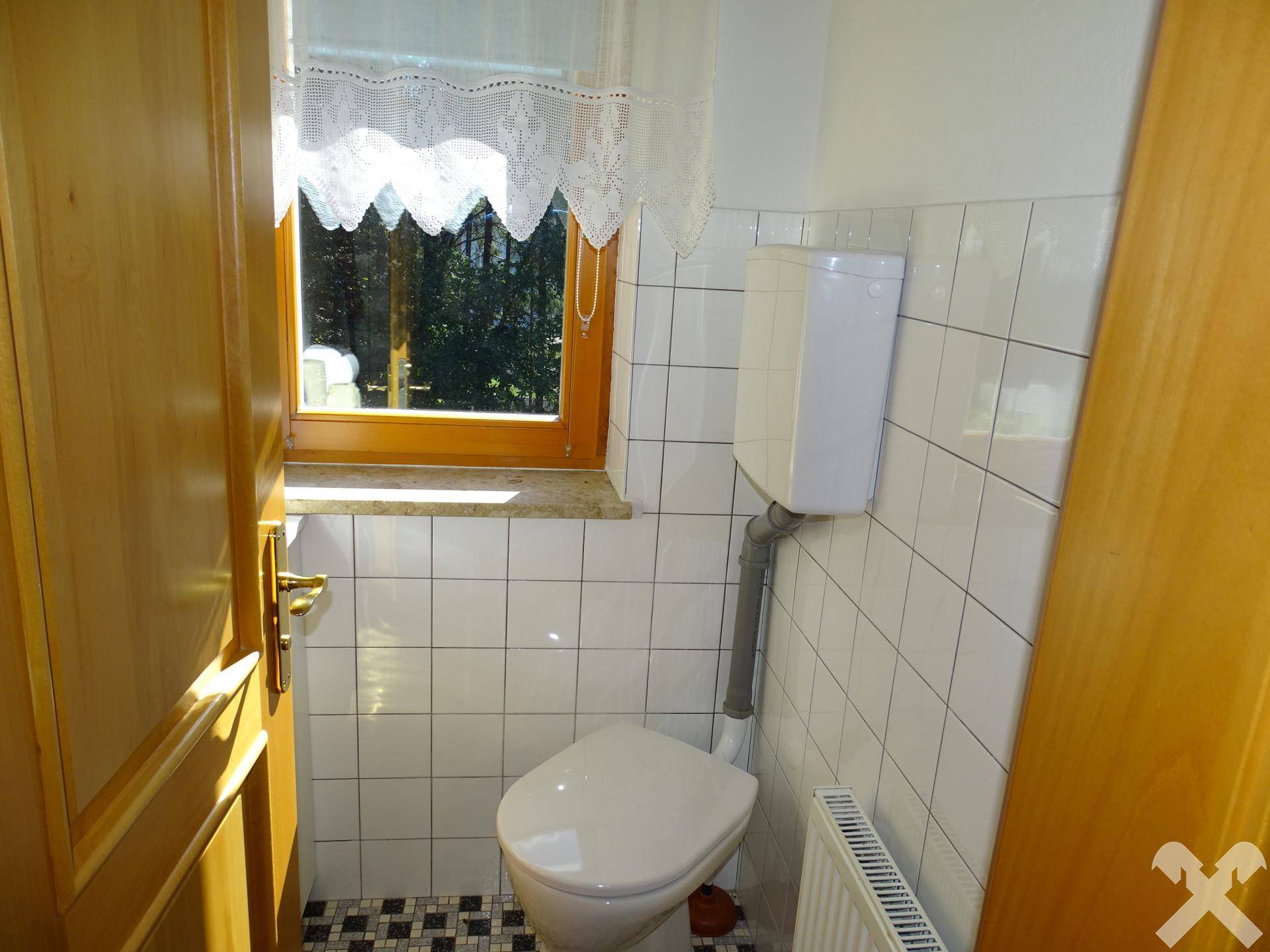 Kleines Gäste-WC mit Fenster, weißen Fliesen und einem einfachen WC-Becken.