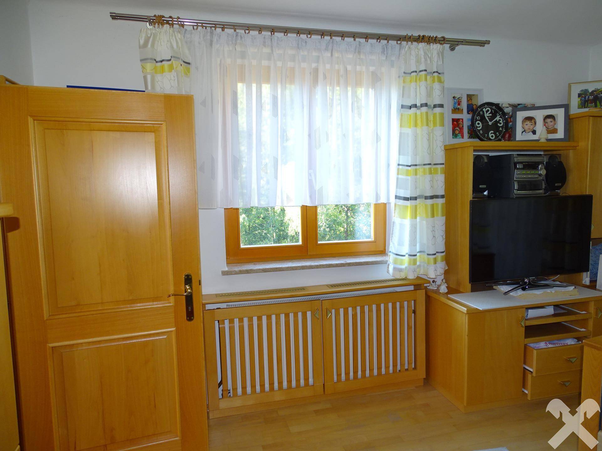 Helles Schlafzimmer mit Fenster, Holzmöbeln und Heizkörper, bietet eine gemütliche Atmosphäre.
