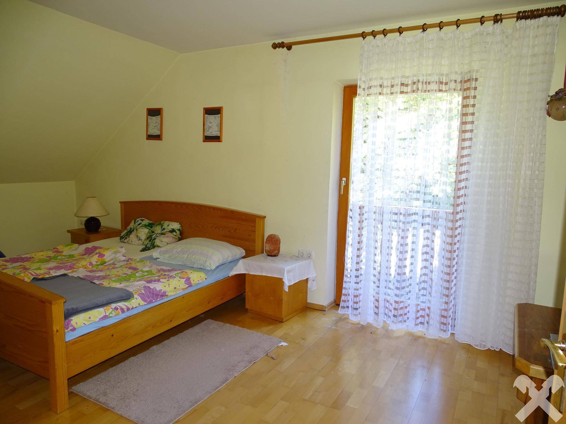 Schlafzimmer mit Holzbett und Zugang zu einem Balkon, unter einer Dachschräge gelegen.