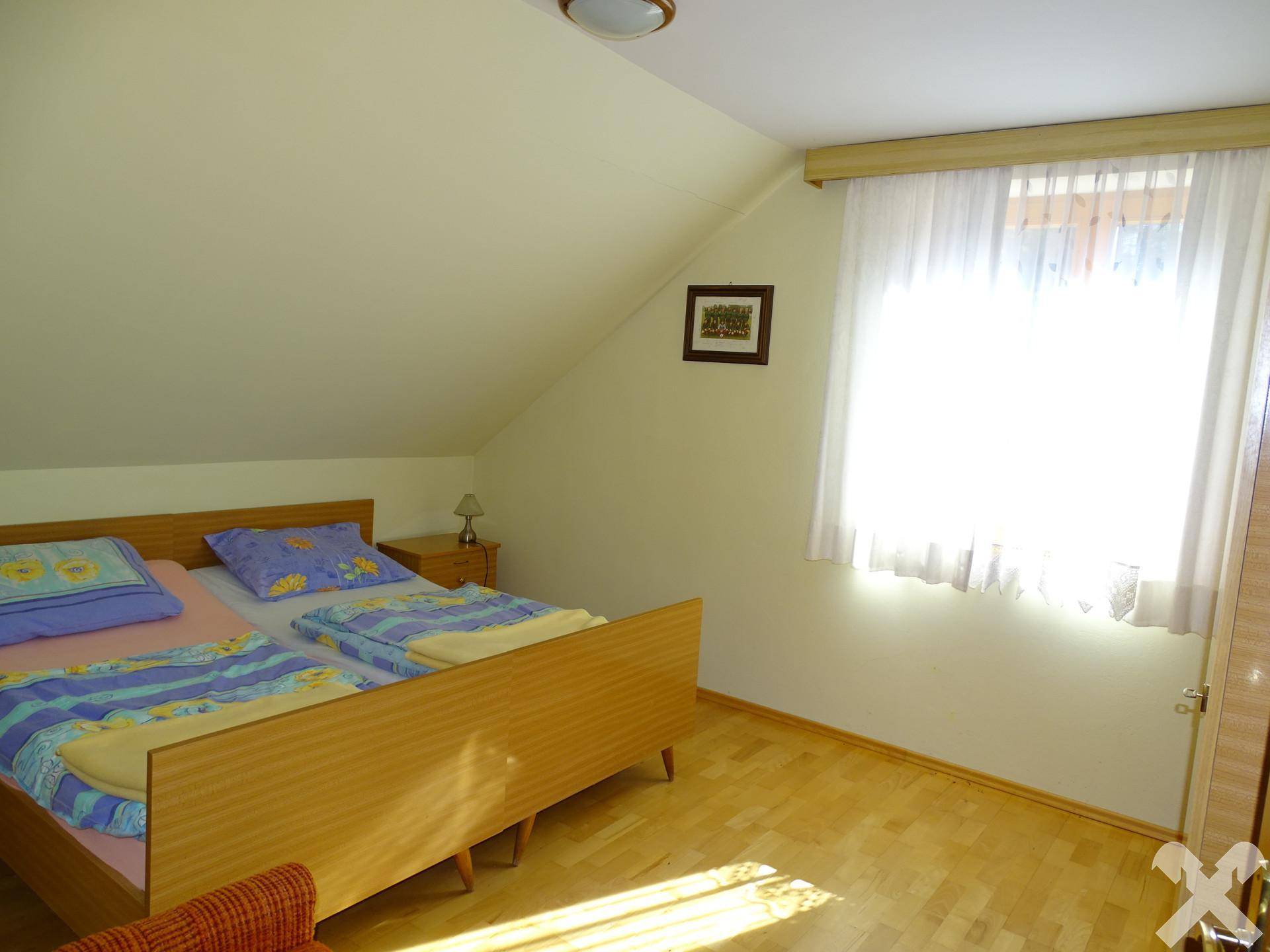 Helles Schlafzimmer mit zwei Einzelbetten und Fenster, unter einer Dachschräge gelegen.