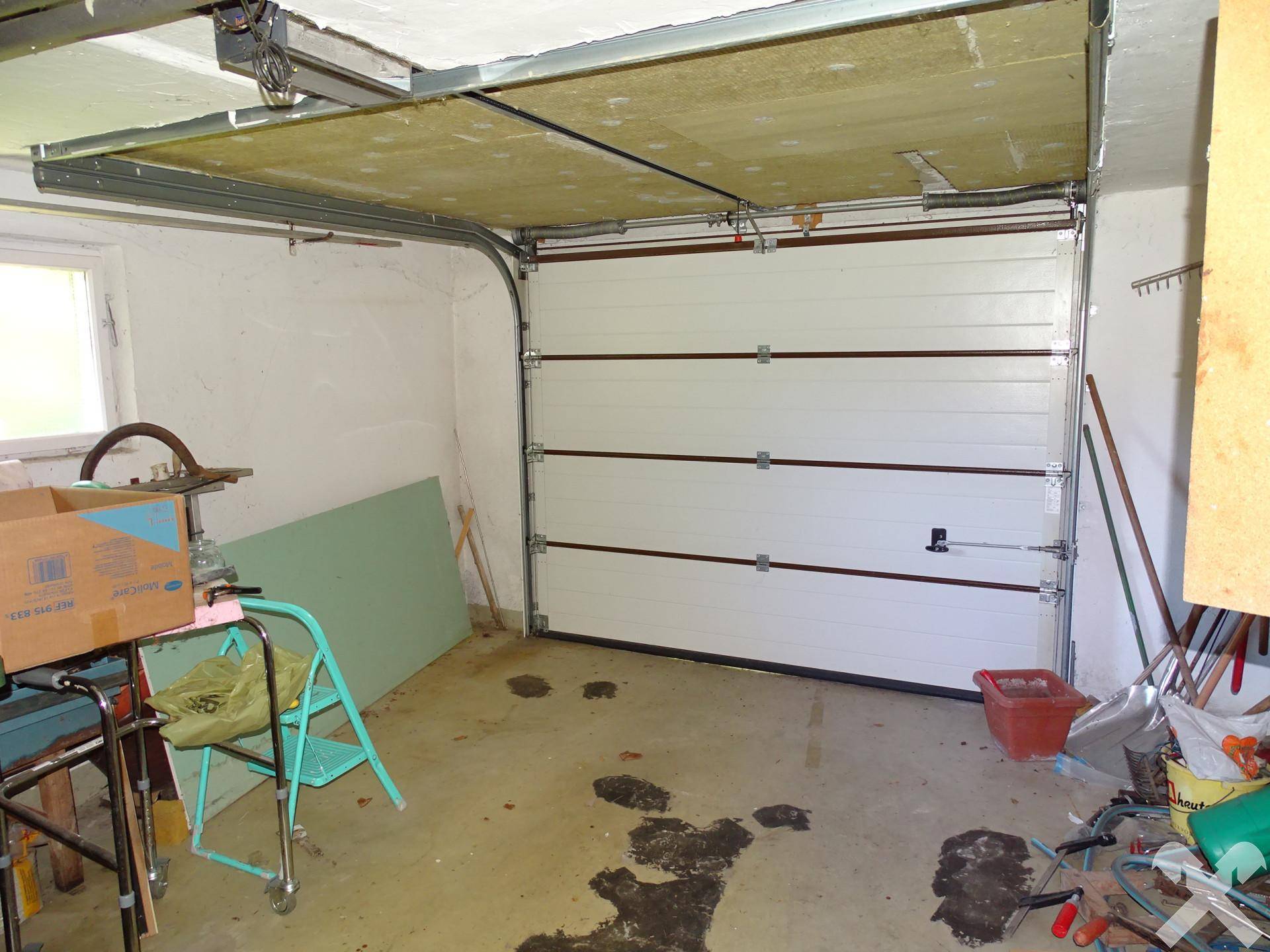 Garage mit weißem Sektionaltor und Stauraum, bietet Platz für ein Fahrzeug und Werkzeuge.