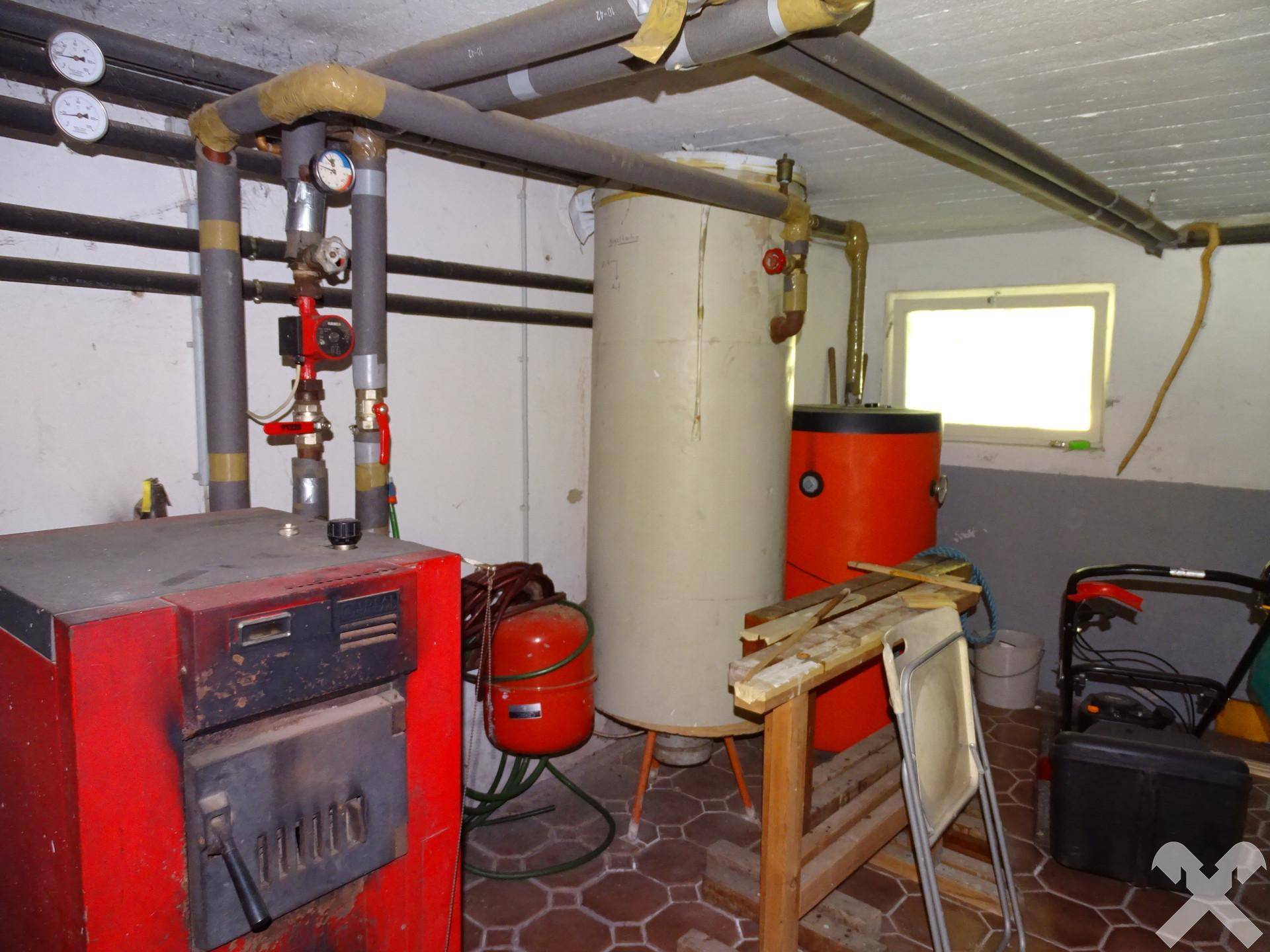 Heizungsraum im Keller mit Boiler, Rohren und einem kleinen Fenster, dient als Technikraum.