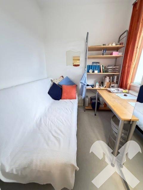 Kleines Büro oder Pausenraum mit einer Liege, Schreibtisch und Regalen für Arbeitsmaterialien.