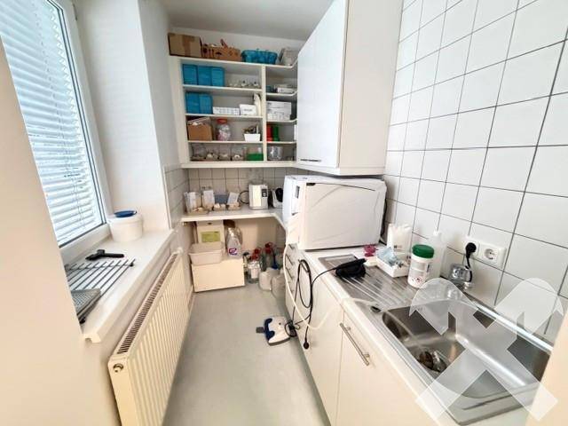 Helle Teeküche mit Fenster, Spülbecken und ausreichend Stauraum für Praxisbedarf und Geräte.
