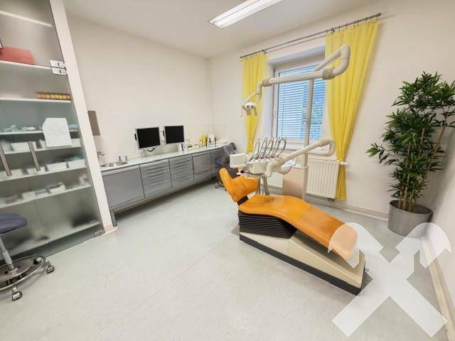 Behandlungszimmer mit zahnmedizinischer Ausstattung, einem Behandlungsstuhl und gelben Vorhängen am Fenster.