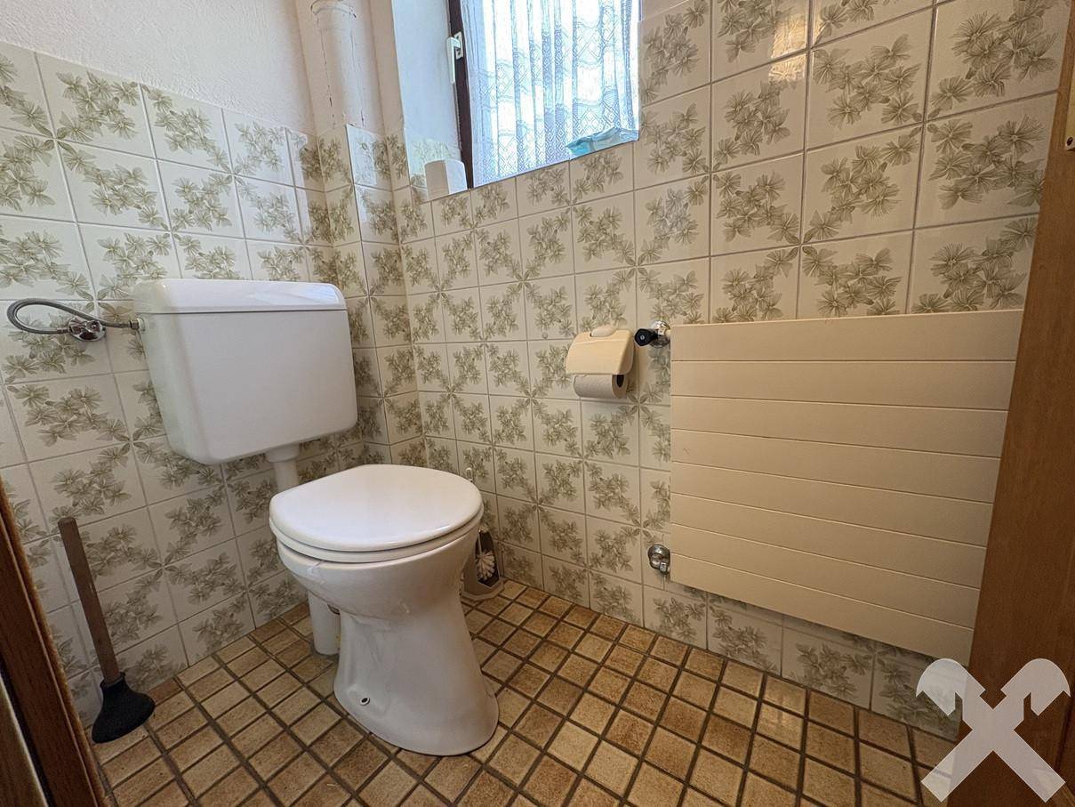 Separate Toilette mit WC und Heizkörper, gefliest in floralem Muster.