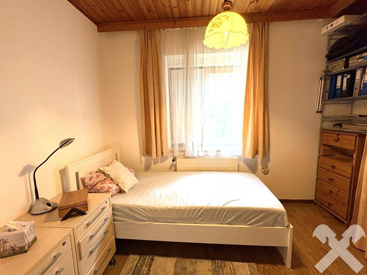 Helles Schlafzimmer mit Einzelbett, Kommode und Fenster mit Vorhängen.