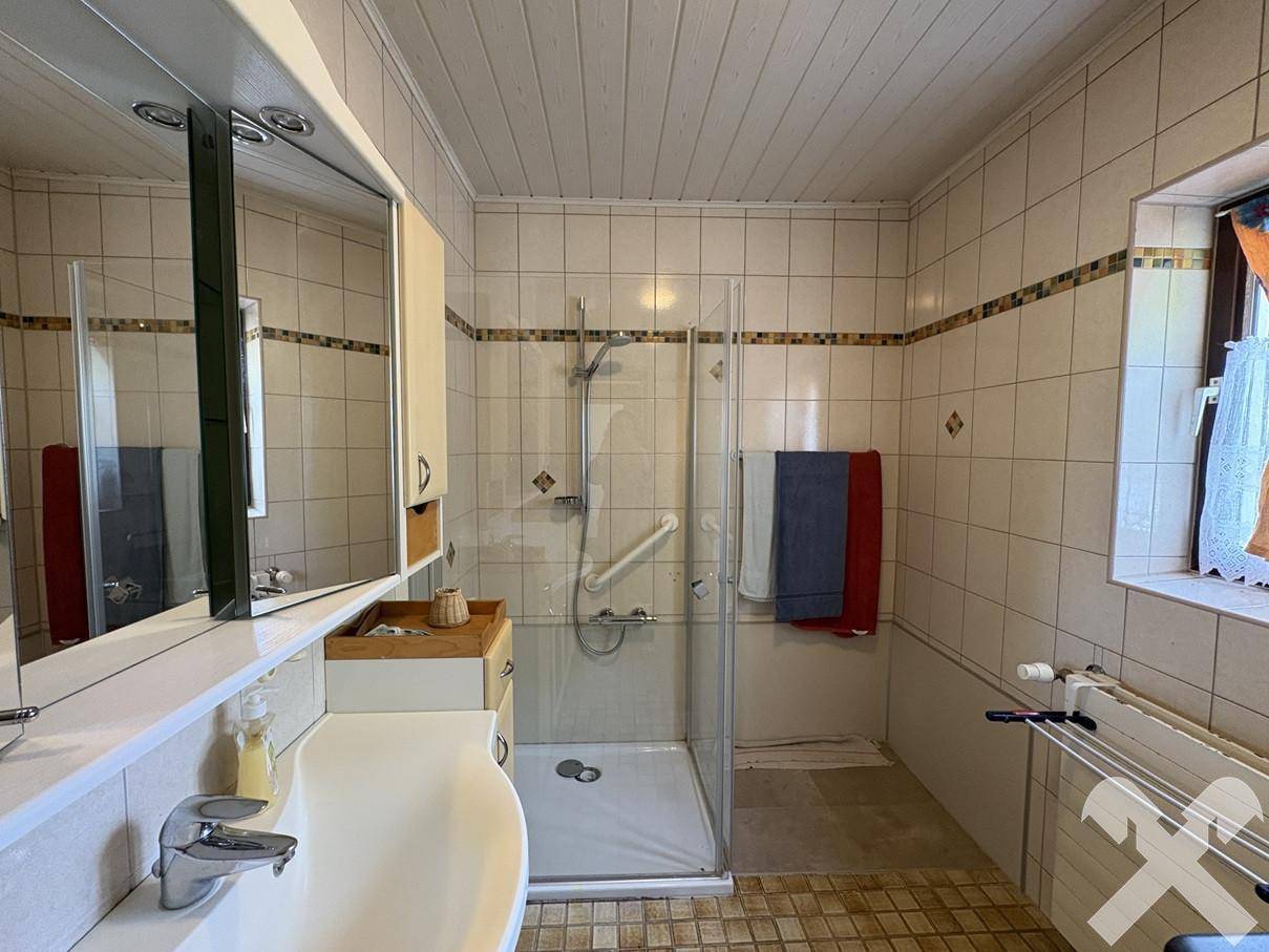 Badezimmer mit Dusche, Waschbecken und Spiegelschrank, hell gefliest.