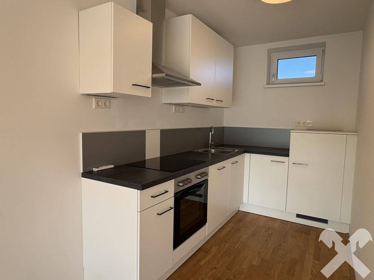 Moderne Küchenzeile mit weißen Schränken, Induktionskochfeld und Backofen, ideal für kompaktes Wohnen.
