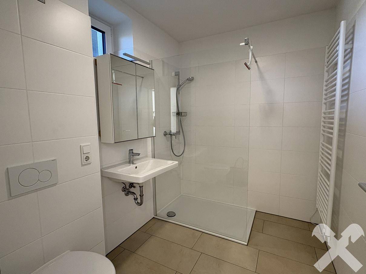 Modernes Badezimmer mit weißen Fliesen, ebenerdiger Dusche und beheiztem Handtuchhalter.