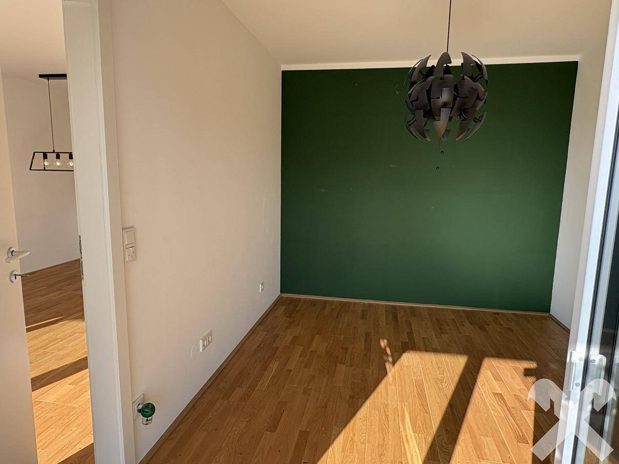 Heller Raum mit Holzboden und einer grünen Akzentwand, geeignet als Essbereich oder Arbeitszimmer.