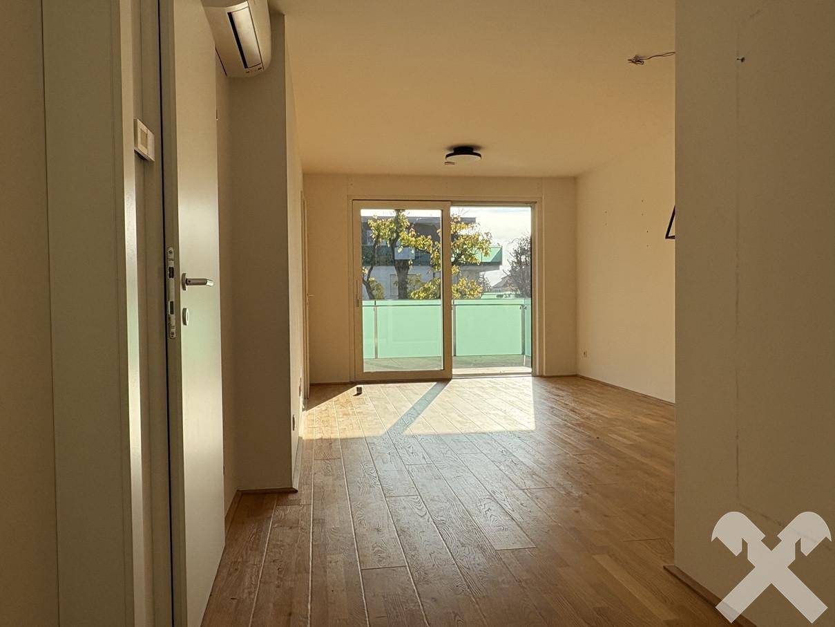 Helles Wohnzimmer mit Holzboden und Zugang zu einem Balkon, ausgestattet mit Klimaanlage.